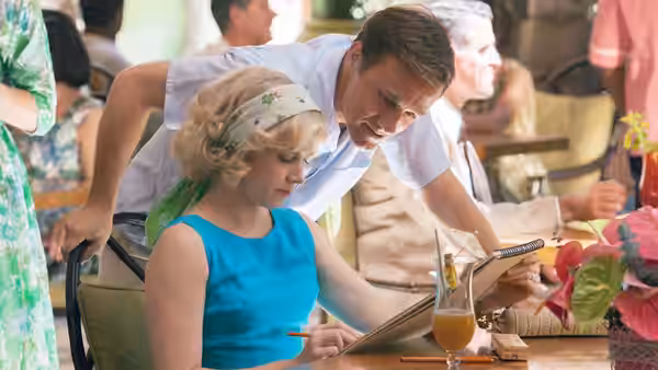 Margaret Keane (Amy Adams) sketches at a café table as Walter Keane (Christoph Waltz) leans over her