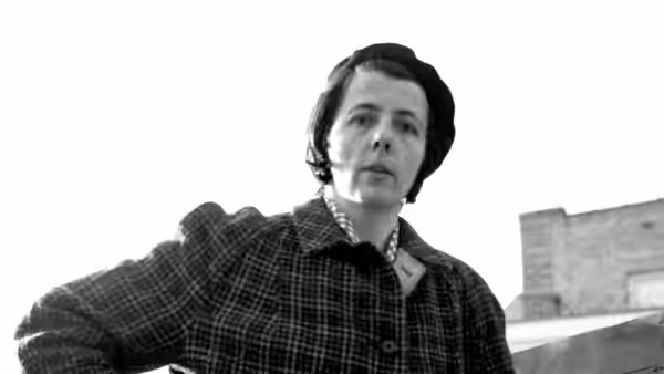 Vivian Maier looks down toward the camera outdoors in a checked coat