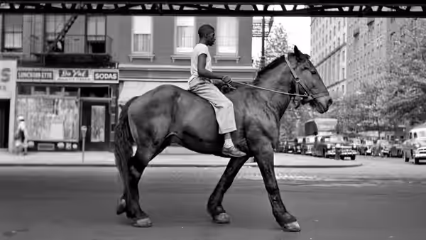 A rider guides a horse across a city street beneath an elevated railway