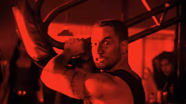 A tattooed man lifts weights with intense focus under red gym lights