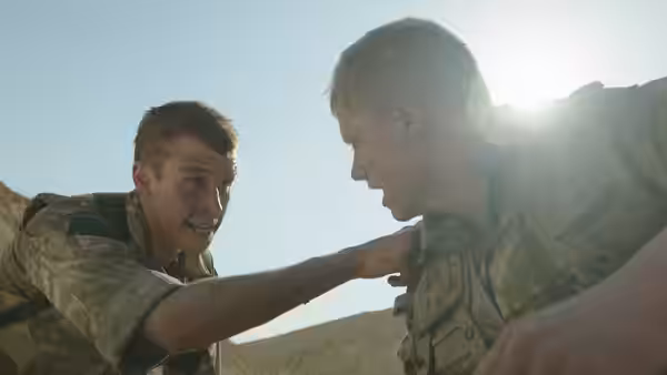 A soldier grips his comrade's shoulder in a rocky desert valley