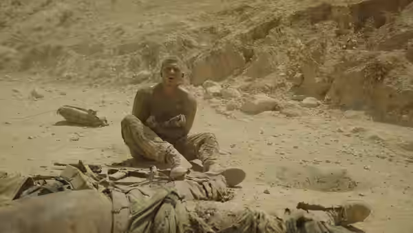 A soldier sits beside a comrade lying on the rocky desert ground