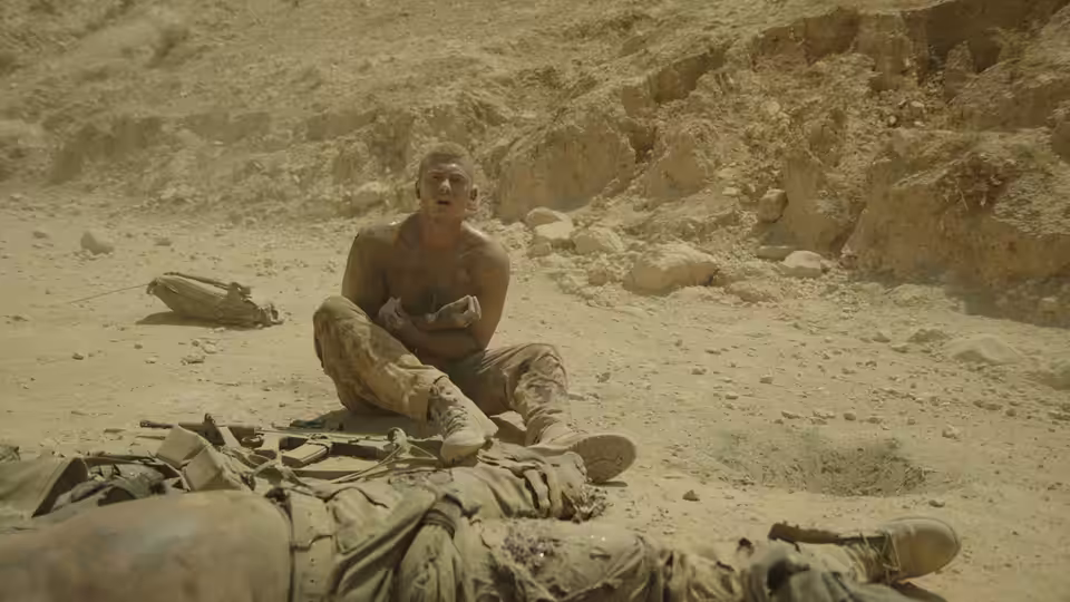 A soldier sits beside a comrade lying on the rocky desert ground