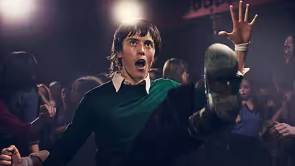 A young man in a green sweater kicks and reaches into a crowded club