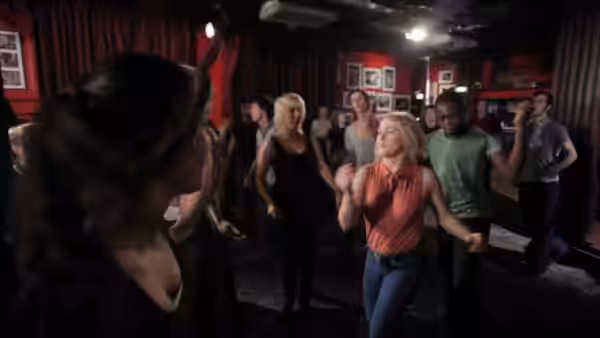 A group of dancers practice steps together in a small club room