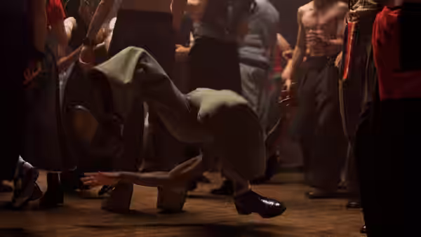 A hooded dancer balances low on one hand among people on the dance floor