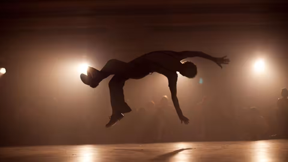 A dancer arches backward in midair beneath spotlights on a dim dance floor