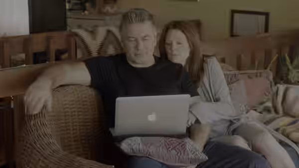 Alice Howland (Julianne Moore) sits close beside John Howland (Alec Baldwin), looking at a laptop
