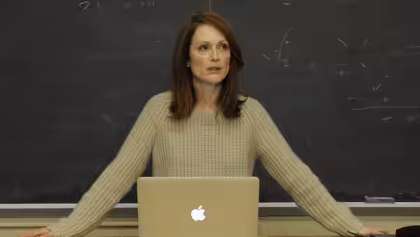 Alice Howland (Julianne Moore) stands behind a laptop in front of a chalkboard