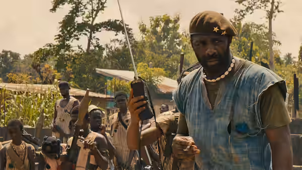 The Commandant (Idris Elba) holds a rifle among soldiers in a village