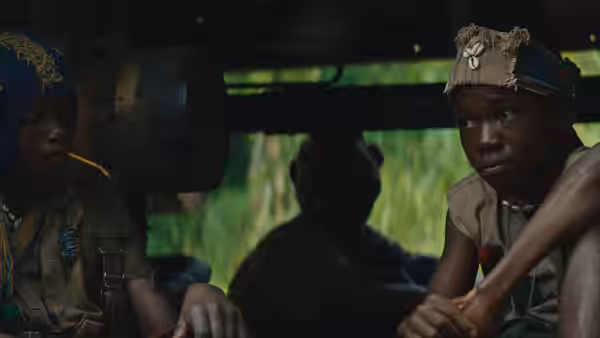 Agu (Abraham Attah) sits inside a shadowy vehicle beside another child soldier