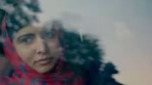 Malala Yousafzai gazes through a window as trees reflect across the glass