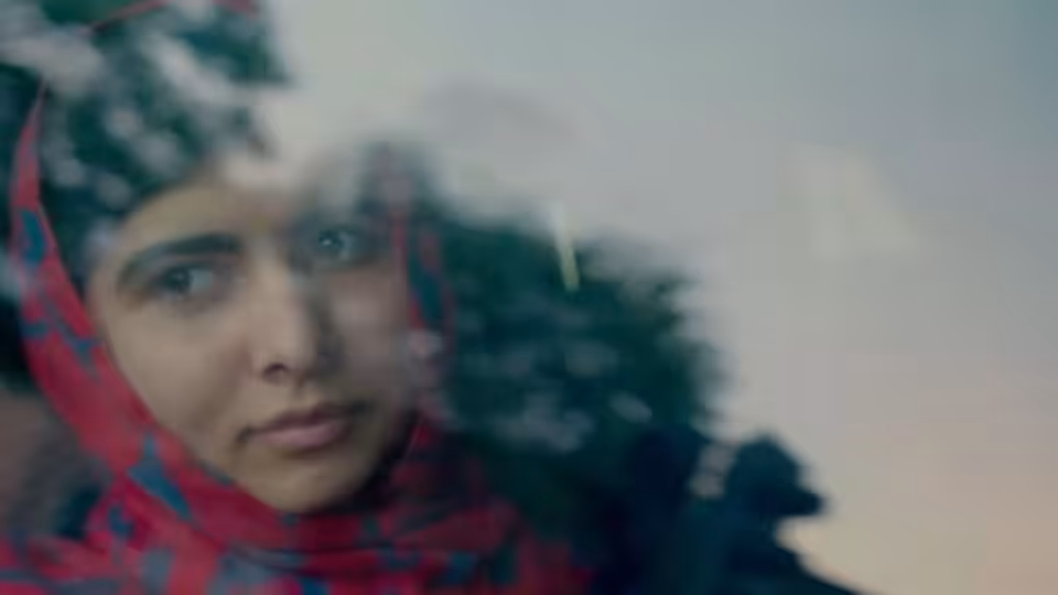 Malala Yousafzai gazes through a window as trees reflect across the glass