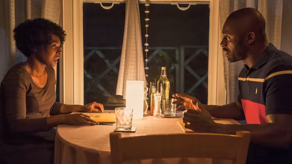Jax (Nadine Marshall) and Mark (Idris Elba) sit across a dining table, talking