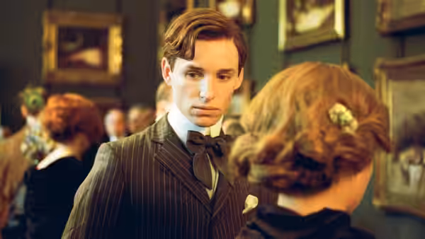 Lili (Eddie Redmayne), dressed in a pinstriped suit, looks toward a woman at a gathering
