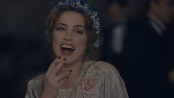 A flower-crowned woman laughs at a gathering, one hand raised near her lips