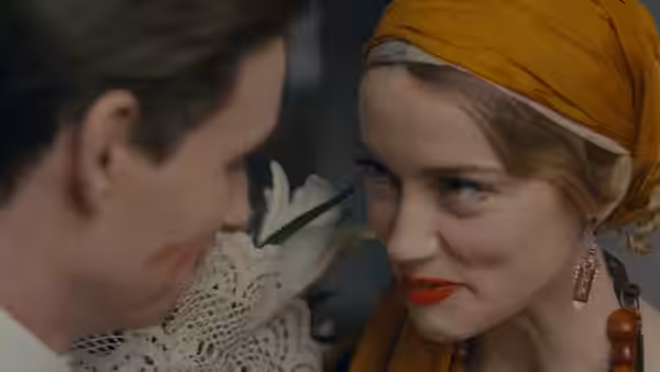 Gerda (Alicia Vikander), wearing an orange headscarf, leans close to a man beside her