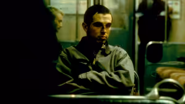 Billy (Charlie Creed-Miles) sitting with arms crossed on a train