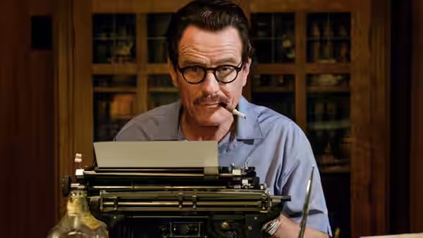 Dalton Trumbo (Bryan Cranston) sits behind a typewriter, smoking a cigarette