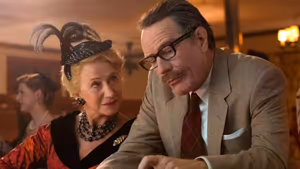 Hedda Hopper (Helen Mirren) and Dalton Trumbo (Bryan Cranston) lean together at a table