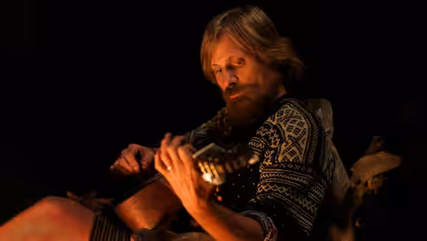 Ben Cash (Viggo Mortensen) plays guitar by the fire in the dark