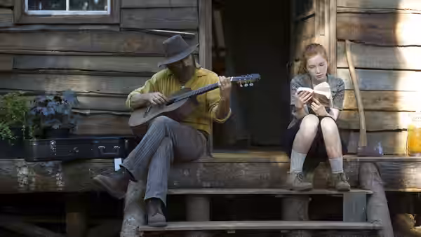 Ben Cash (Viggo Mortensen) plays guitar on a cabin step as Vespyr (Annalise Basso) reads