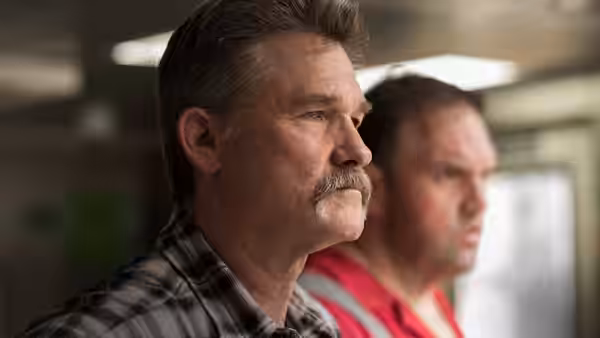 Jimmy Harrell (Kurt Russell) stands in profile beside a colleague indoors