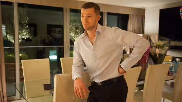 Jason (Russell Tovey) leans against a dining chair in a modern apartment