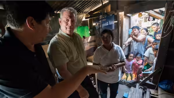 Al Gore visits a crowded home with local residents and a group gathered outside