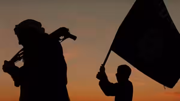 A silhouetted man films as another raises a black flag at sunset