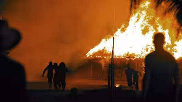 Silhouetted figures flee as a building burns in the night