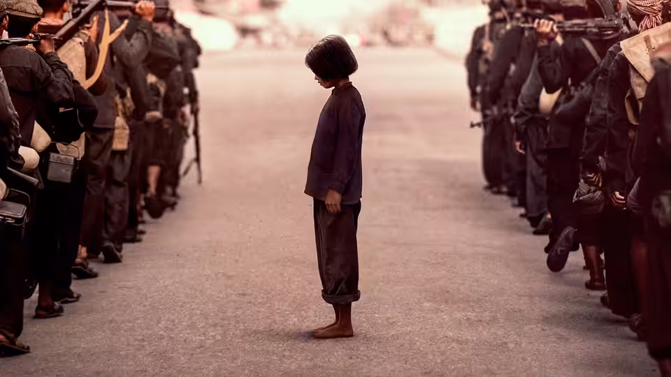 A child stands with head bowed between two lines of armed soldiers