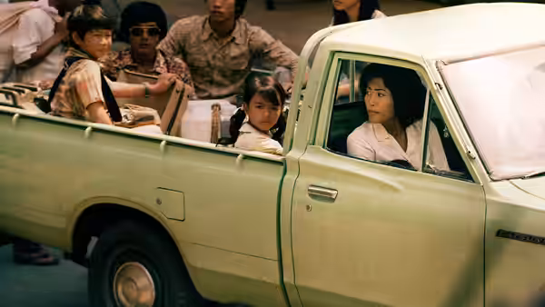 A woman and children ride in a pickup truck through a crowded street