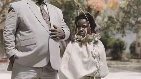 Shula stands beside a suited man, tethered by a ribbon