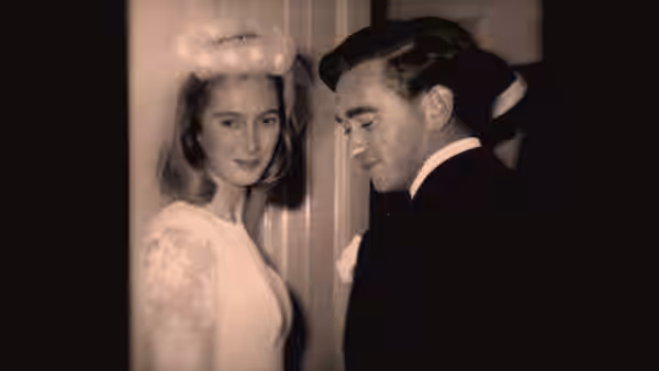 A young woman in a white dress stands beside a man in formalwear