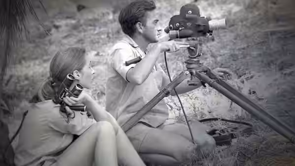 A woman and a man operate cameras on tripods in the field