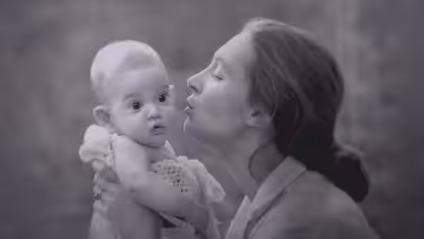 A woman kisses a baby held in her arms outdoors