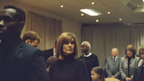 Ivanna (Siobhan Finneran) stands among congregation members in a meeting hall