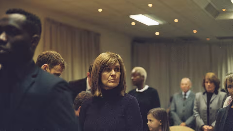 Ivanna (Siobhan Finneran) stands among congregation members in a meeting hall
