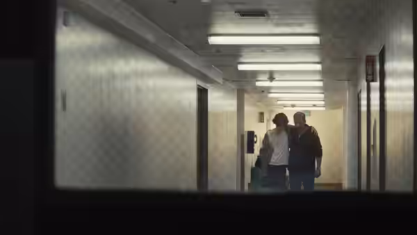 David Sheff and Nic walk together down a fluorescent-lit institutional hallway