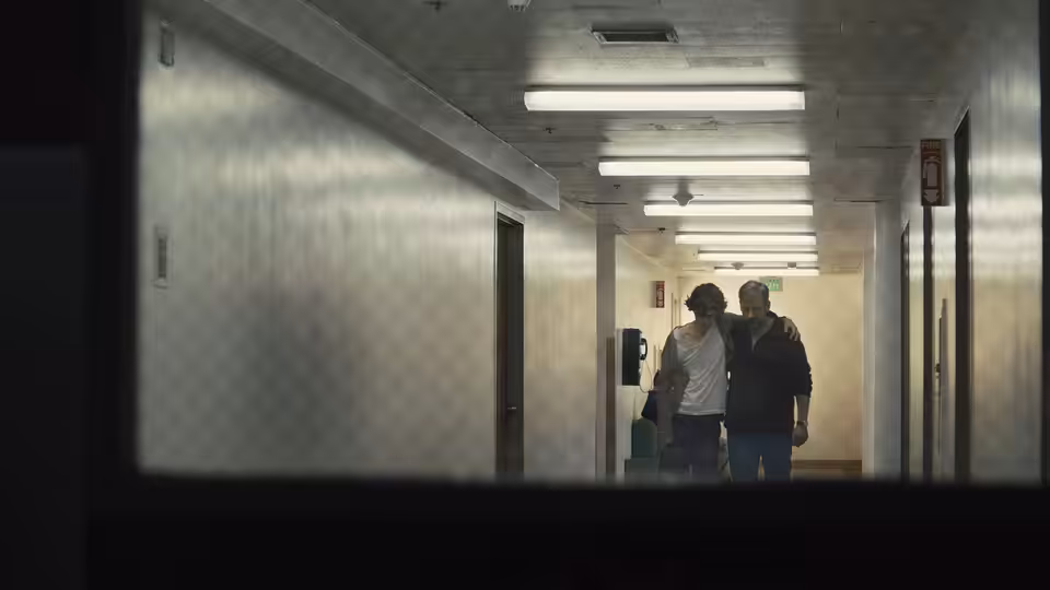 David Sheff and Nic walk together down a fluorescent-lit institutional hallway