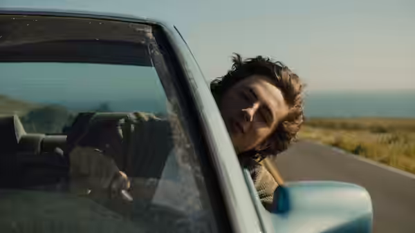 Nic leans out of a car window as it travels along a country road