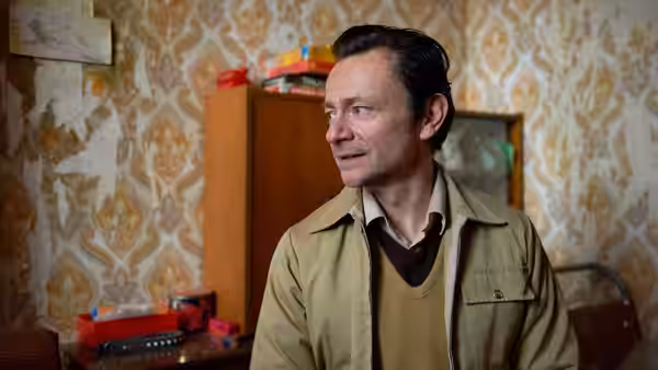 Ray (Justin Salinger) stands in a wallpapered room, glancing to the side