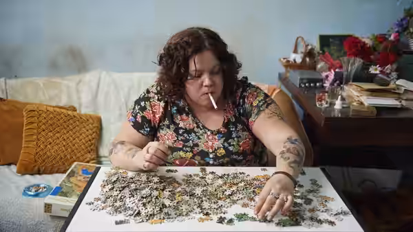Liz (Ella Smith) works on a jigsaw puzzle with a cigarette in her mouth
