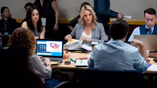 Megyn Kelly (Charlize Theron) reviews papers during a meeting around a conference table