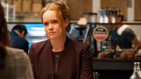 A young woman sits at a restaurant table, listening to someone across from her