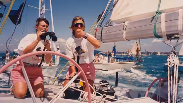 Two women aboard a yacht scan the water with binoculars as other boats pass
