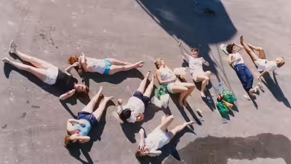 A group of women lies on a marina dock beside a yacht’s shadow