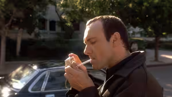Verbal (Kevin Spacey) lighting a cigarette beside a parked car