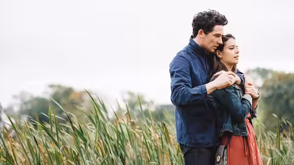 Jake (Josh O'Connor) stands behind Elena (Laia Costa) in a field
